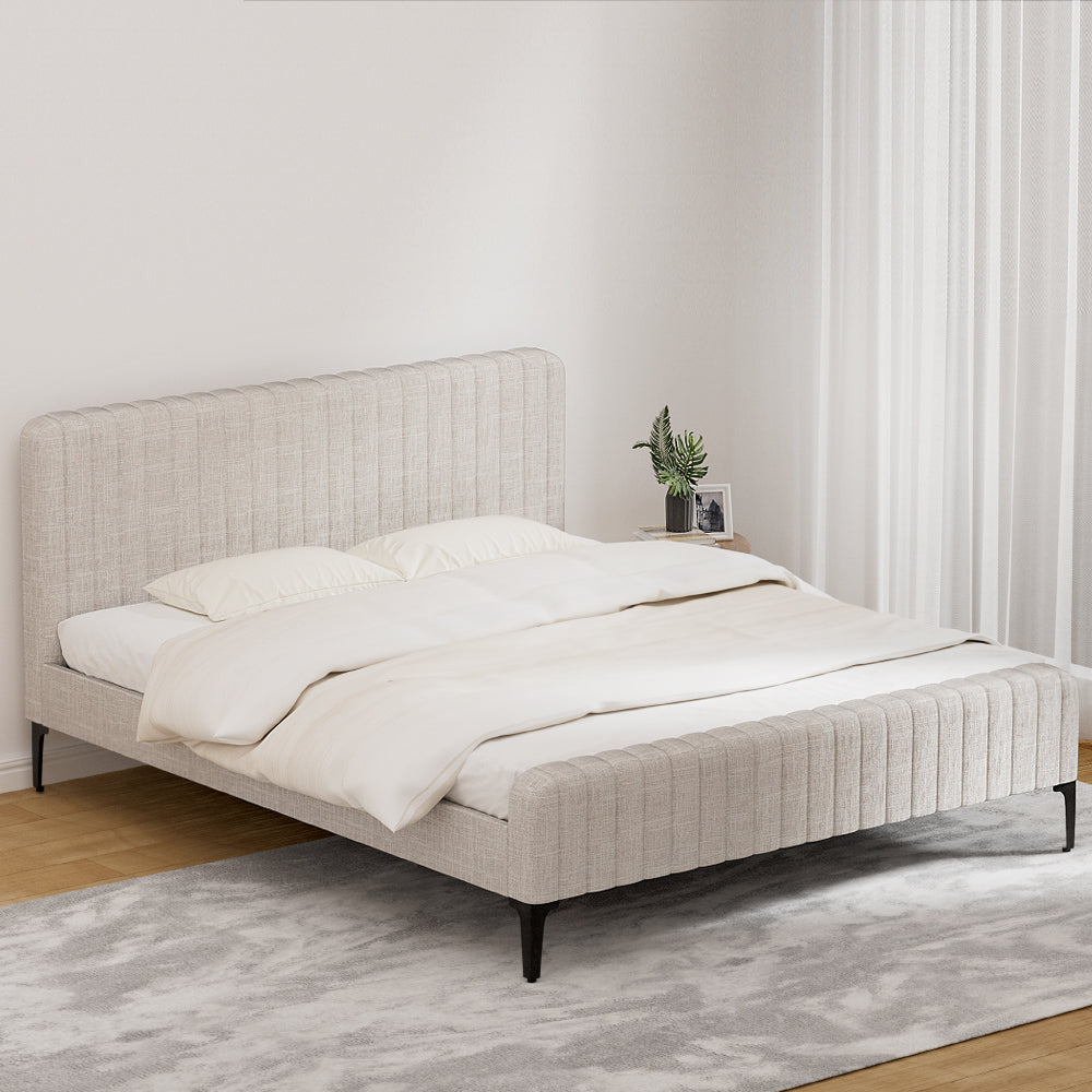 Burleigh King Bed Frame Beige with vertical tufted headboard, faux linen upholstery, slim black legs, and white bedding on gray rug