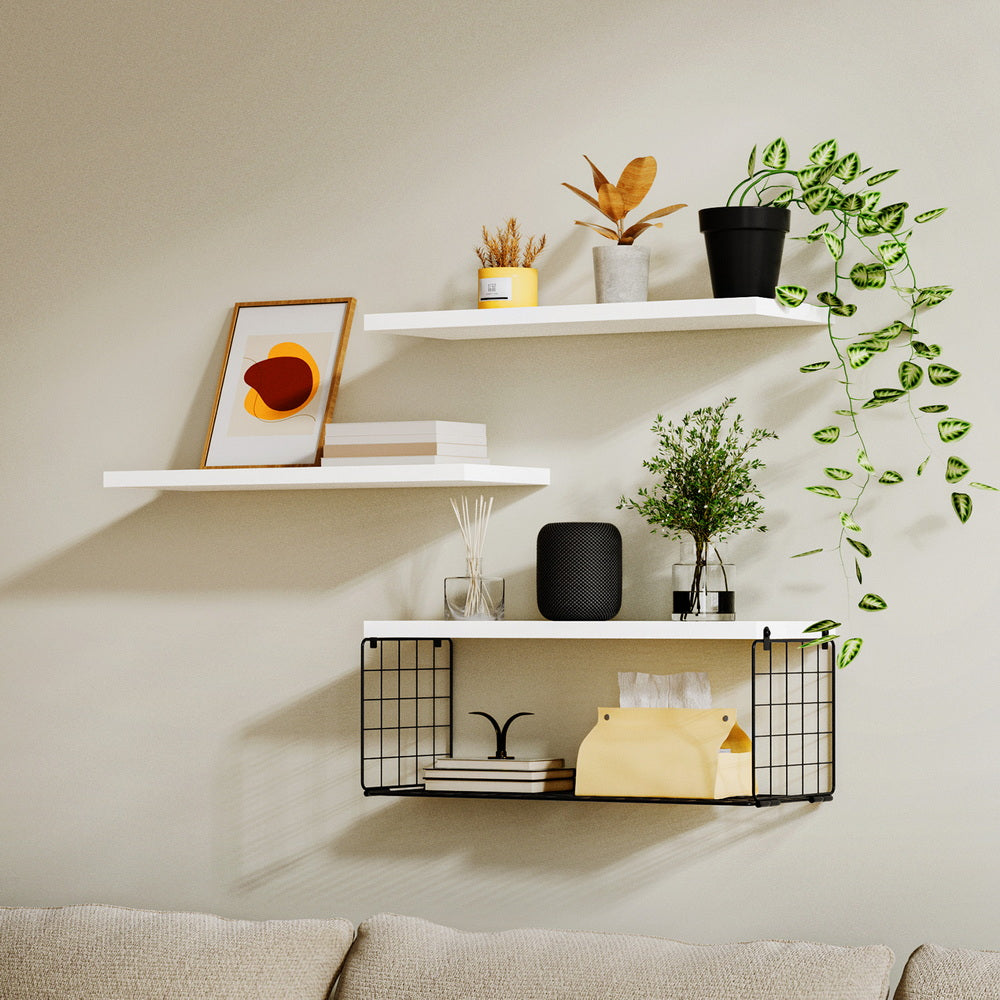 Floating Wall Shelf Set of 3 White with decorative plants, books, framed art, and metal storage basket above beige sofa
