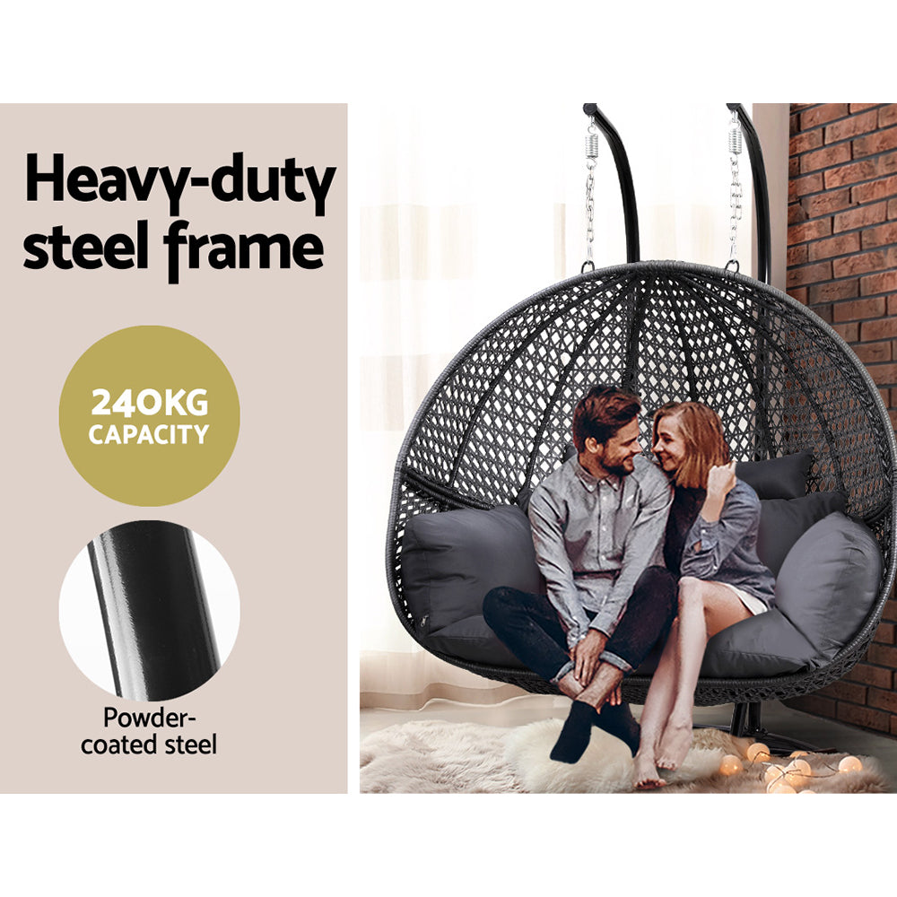 Outdoor Swing Chair Hanging Rattan Patio Furniture Pod Stand Cushion 2 Seater with black metal frame and gray cushions with couple sitting inside