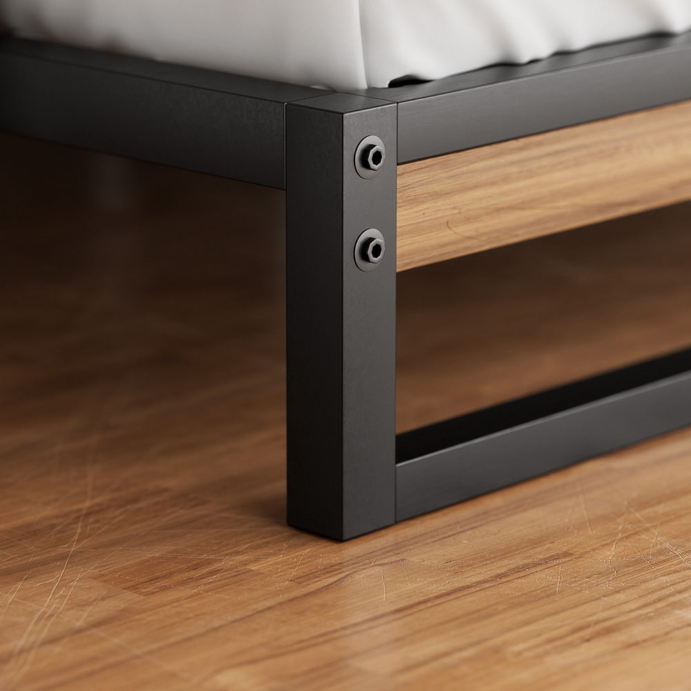 Close-up of black metal and wood frame corner on the Stockton Metal Queen Bed Frame showing sturdy construction on wooden floor