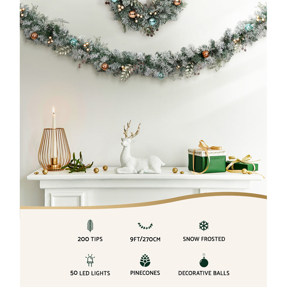 2.7m Christmas Garland with LED Lights Snowy Decoration Xmas Party featuring pinecones, decorative balls, and warm white lights on mantel.