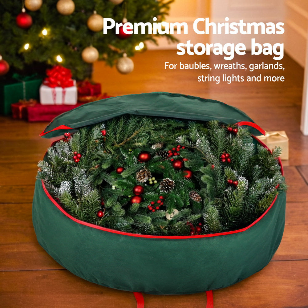 Green Christmas Garland Wreath Storage Bag Baubles Ornaments Container filled with holiday wreath, shown on wooden floor near decorated tree