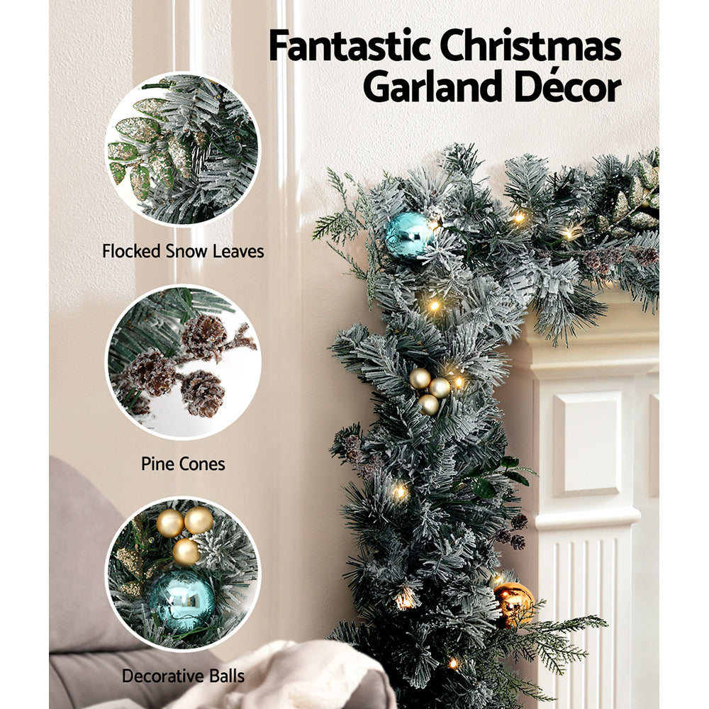 2.7m Christmas Garland with Wreath Set LED Lights Snowy Xmas Decor with flocked leaves, pine cones, and decorative baubles on mantel