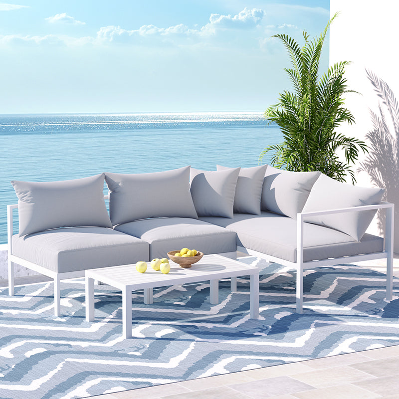 Airlie 4 Seat Aluminium Outdoor Sofa and Table Set White with cushions, coffee table, and decorative plant by the water