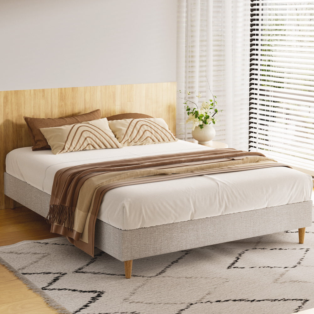 Zora Double Bed Frame Base Beige with upholstered base, wooden legs, and neutral bedding in a bright bedroom setting