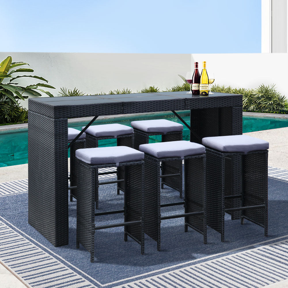 7-Piece Outdoor Bar Set Dining Table Stools Wicker Patio Setting in black with cushioned stools by the poolside on rug
