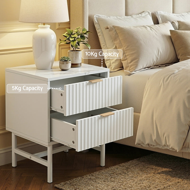 Bedside Table 2 Drawers - White with textured drawer fronts, gold handles, and sturdy legs beside a bed with bedding and lamp