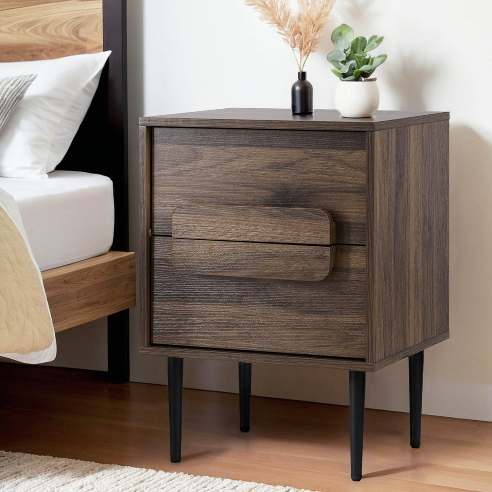 Bedside Table Nightstand 2 Drawers - Walnut with black legs and decorative plants on top by a wooden bed frame
