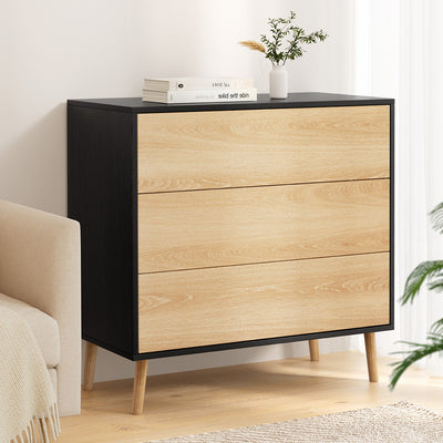 3 Chest of Drawers Dresser Table Black&Pine with three drawers, wooden legs, and black frame in a bright bedroom setting