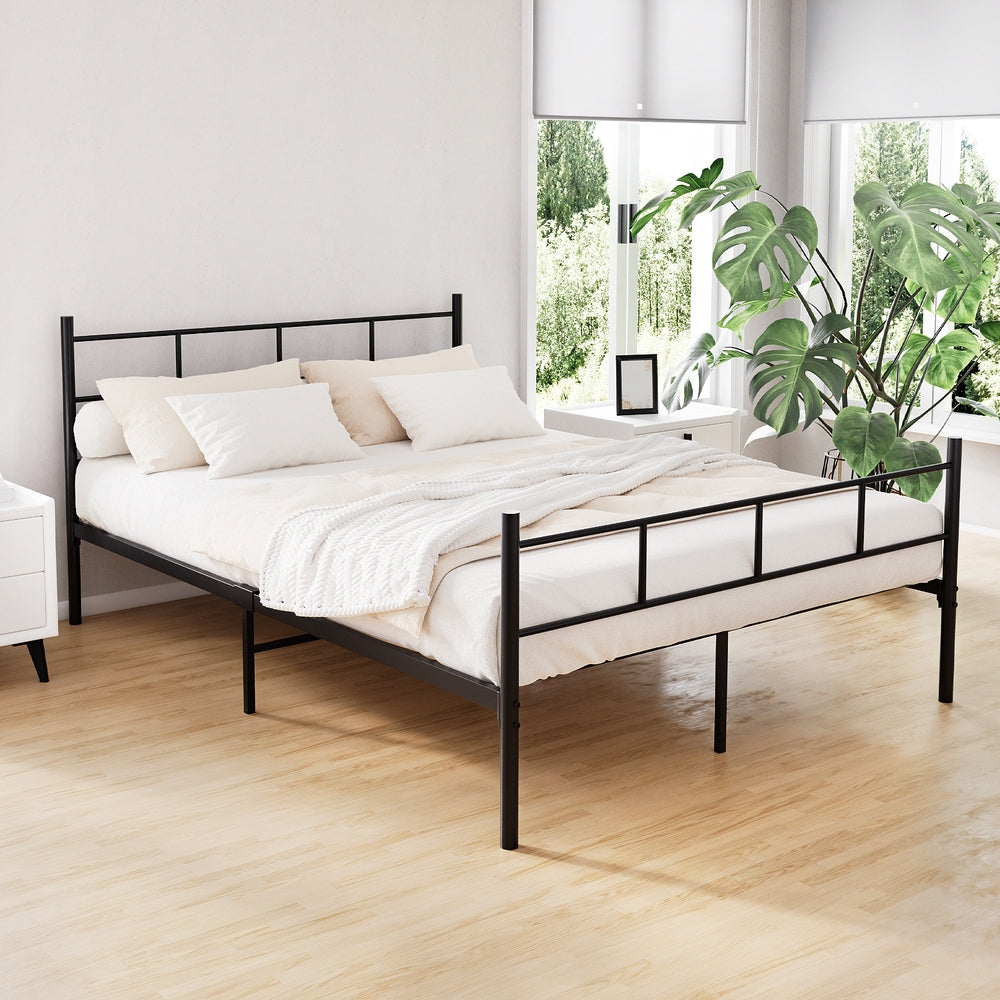 Wategos Metal Double Bed Frame Black in a bright bedroom with white bedding, bedside tables, and large green plant
