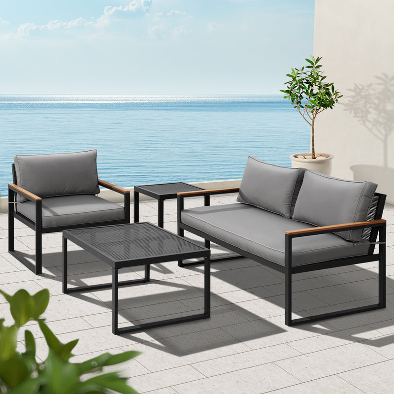 3 Seater Corner Steel Modular Lounge Setting with gray cushions, black frame, wooden armrests, coffee and side tables on patio by the sea