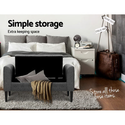 Fabric Storage Ottoman - Grey with lifted lid showing storage space, placed in bedroom with bed and nightstand