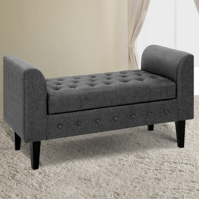 Fabric Storage Ottoman - Grey with tufted seat, button accents, and wooden legs, shown in a bedroom setting on carpet
