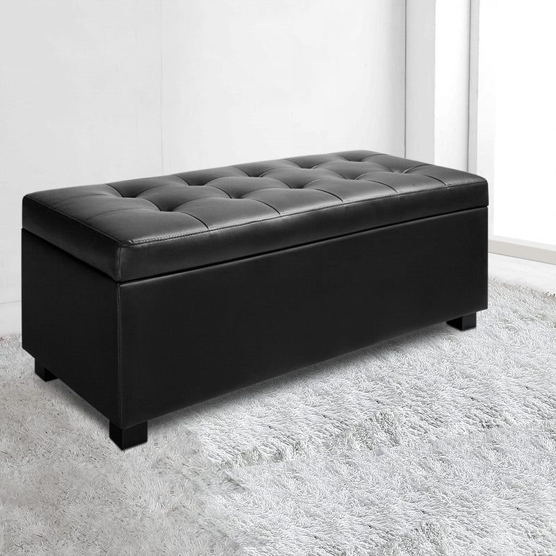 PU Leather Storage Ottoman - Black with tufted top and storage inside, set on black feet on a light rug background