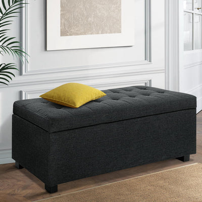 Premium Storage Ottoman - Charcoal with tufted faux linen fabric, sturdy legs, and decorative yellow cushion in elegant bedroom setting