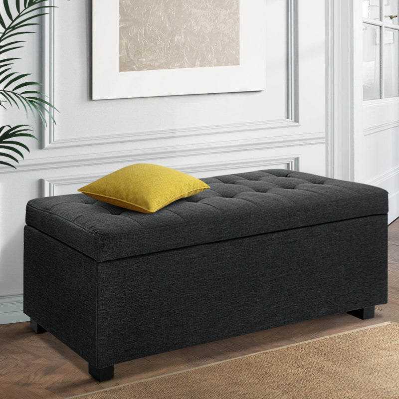 Premium Storage Ottoman - Charcoal in faux linen fabric with tufted top and black feet, styled with a yellow pillow in bedroom setting