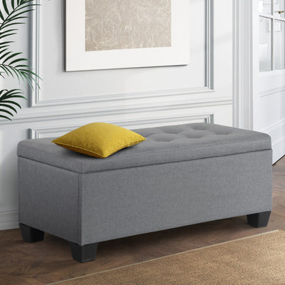 Large Fabric Storage Ottoman - Grey with tufted top and black legs, styled with a yellow cushion in bedroom setting