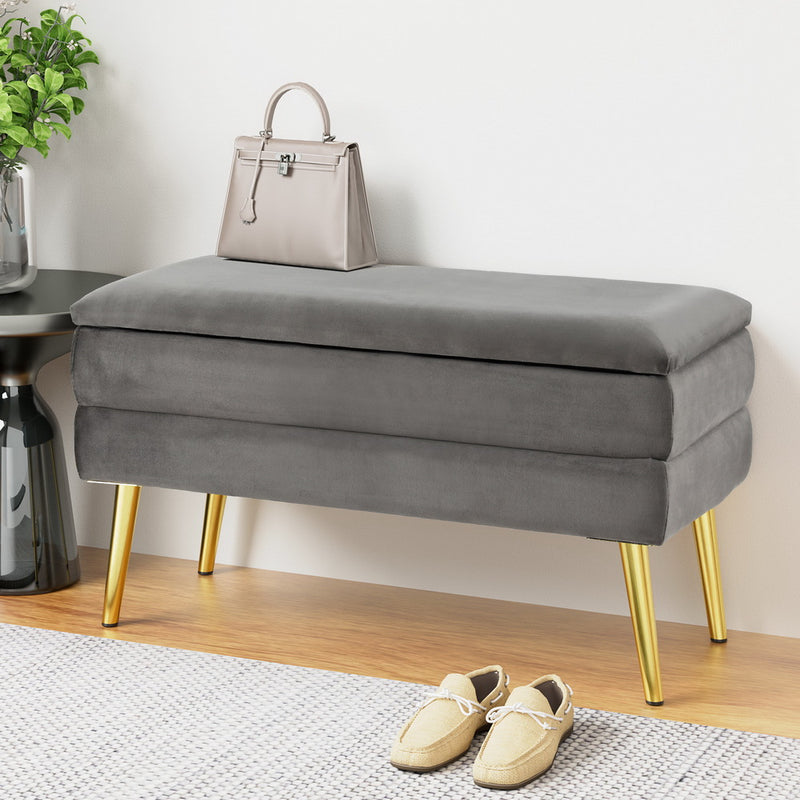 Ottoman Storage Foot Stool Velvet Grey with plush velvet upholstery, gold legs, and horizontal stripe design in bedroom setting