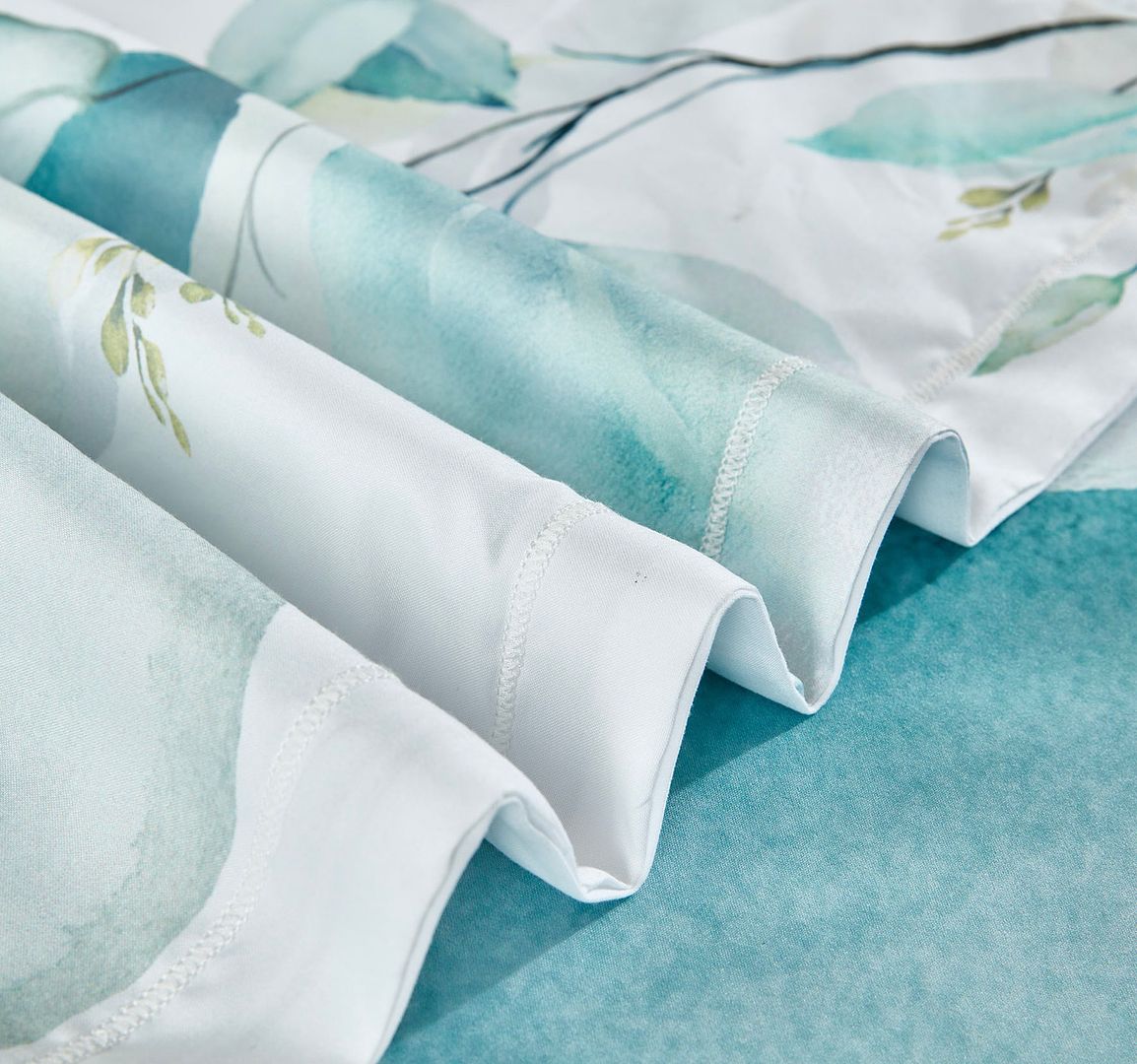 Close-up of Angelis Leaves Quilt Cover Set - King Size fabric folds in soft green and white tones on teal surface