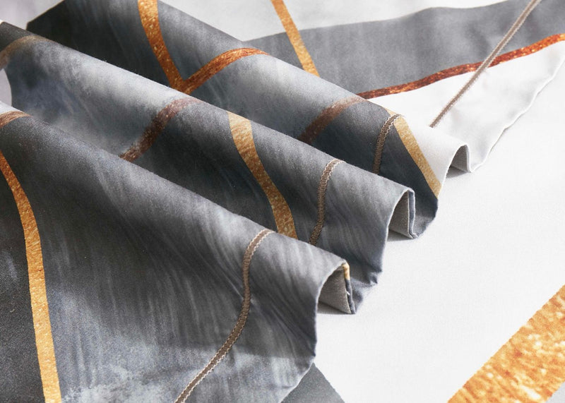 Close-up of folded fabric featuring gray and gold geometric patterns from the Dakuta Quilt Cover Set - King Size