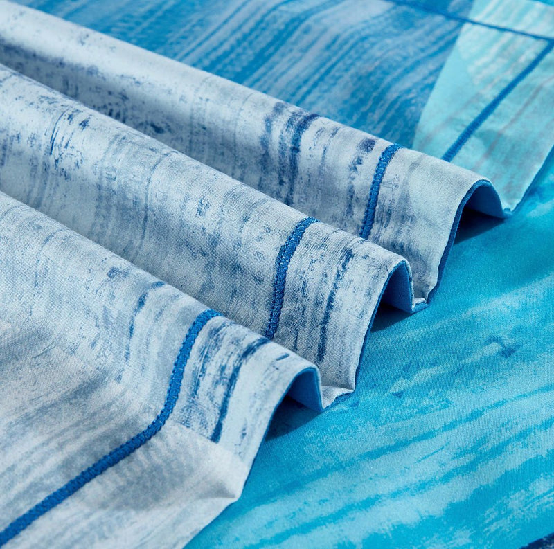 Close-up of blue patterned fabric folds from the Mondrian Quilt Cover Set - Queen Size on a blue bed surface