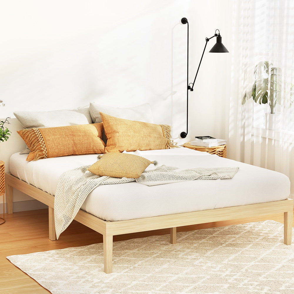 Bruno Minimalist Double Solid Pinewood Bed Frame in natural wood finish displayed in bright bedroom setting with textiles and wall lamp