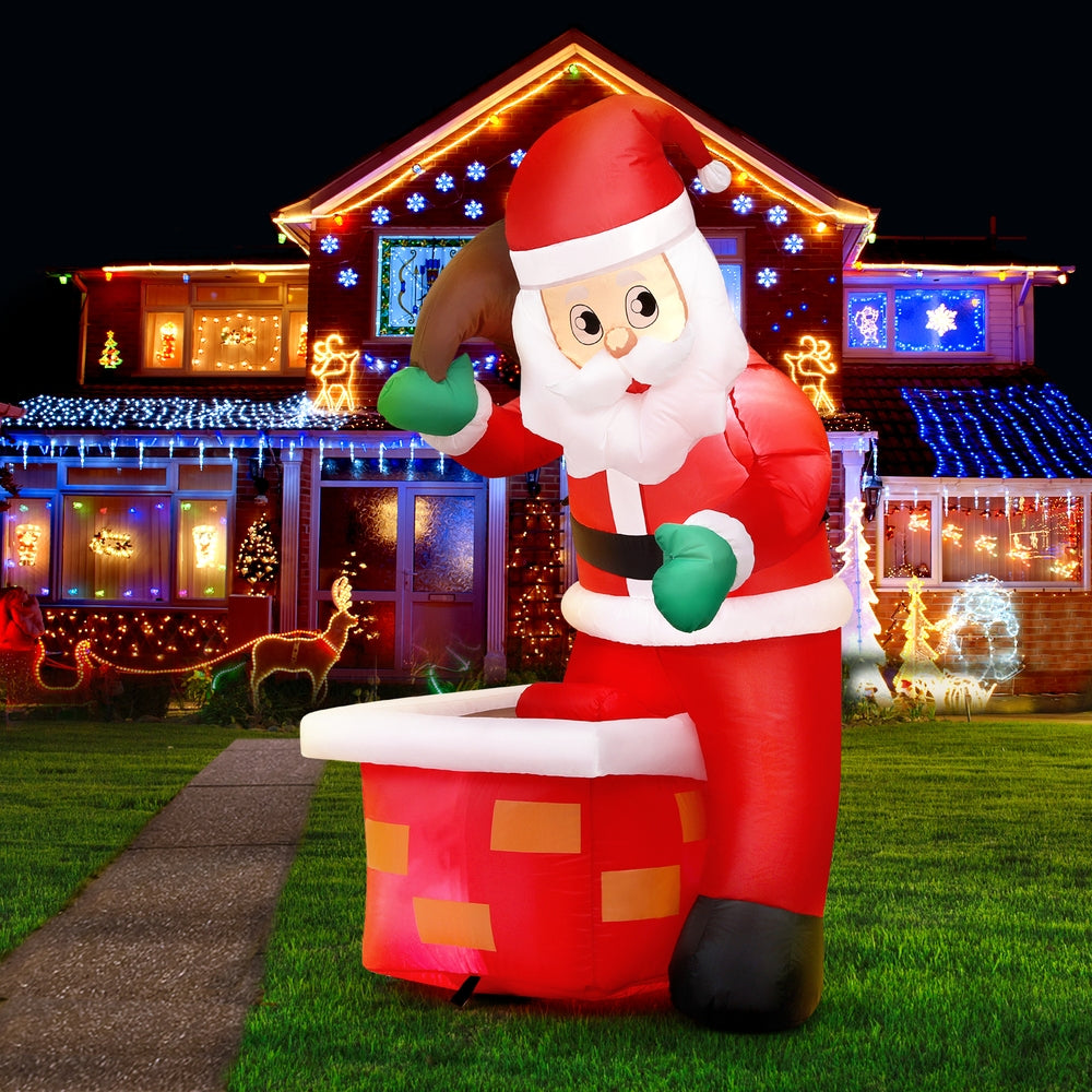 Christmas Inflatable Santa Illuminated Decorations with glowing lights, standing next to a chimney in a festive yard at night